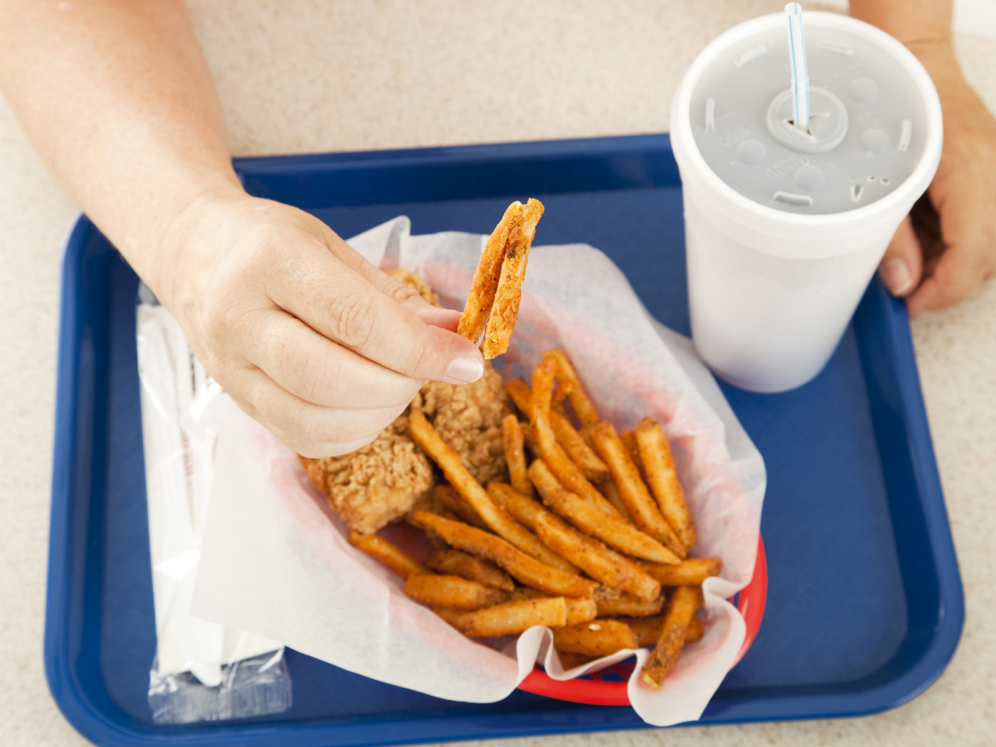A plate of greasy fast food, with the customer holding up a greasy french fried potato to the camera.  Focus on the hand and the fry.