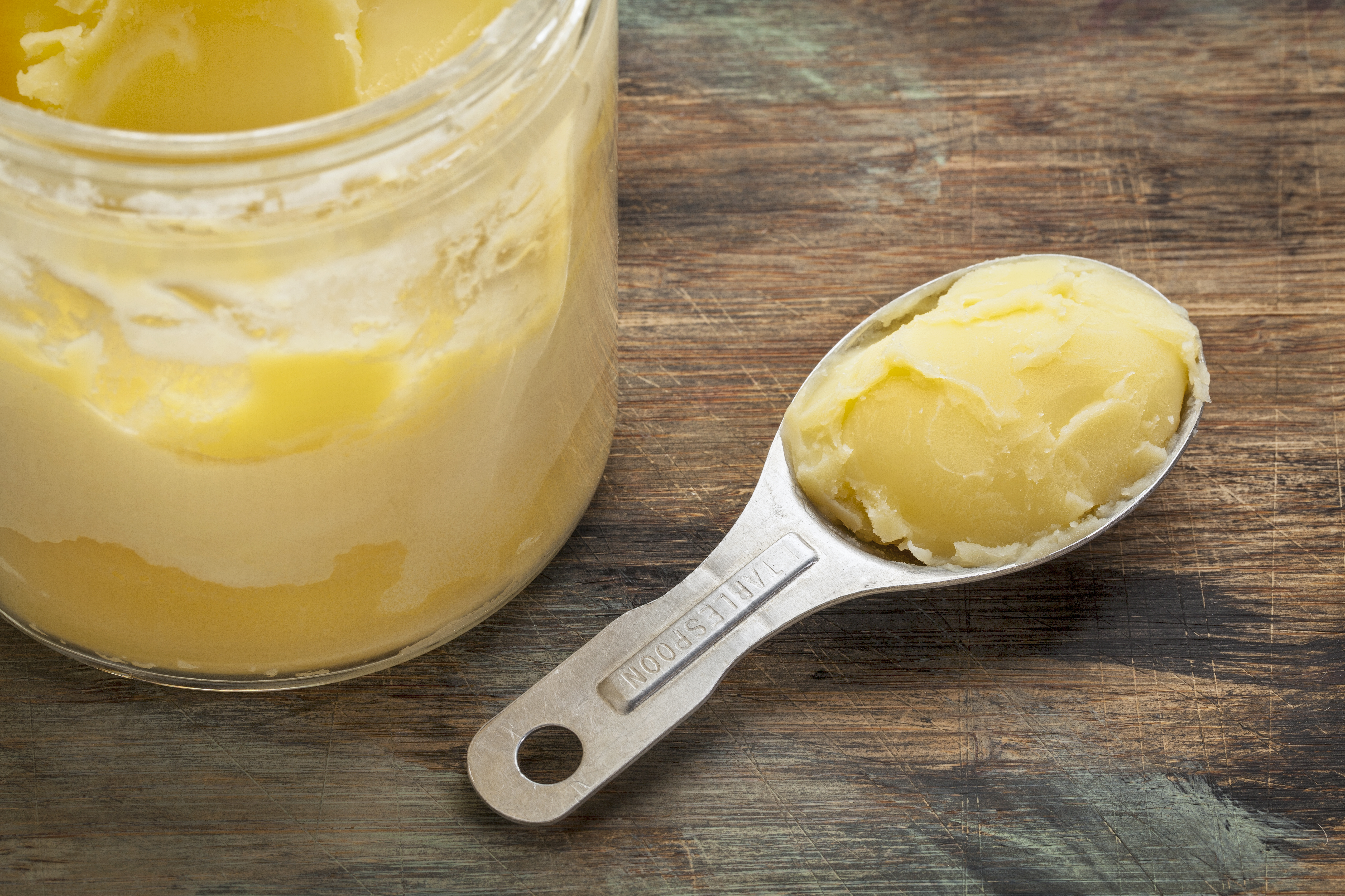jar and measuring tablespoon of ghee - clarified butter on grunge wood
