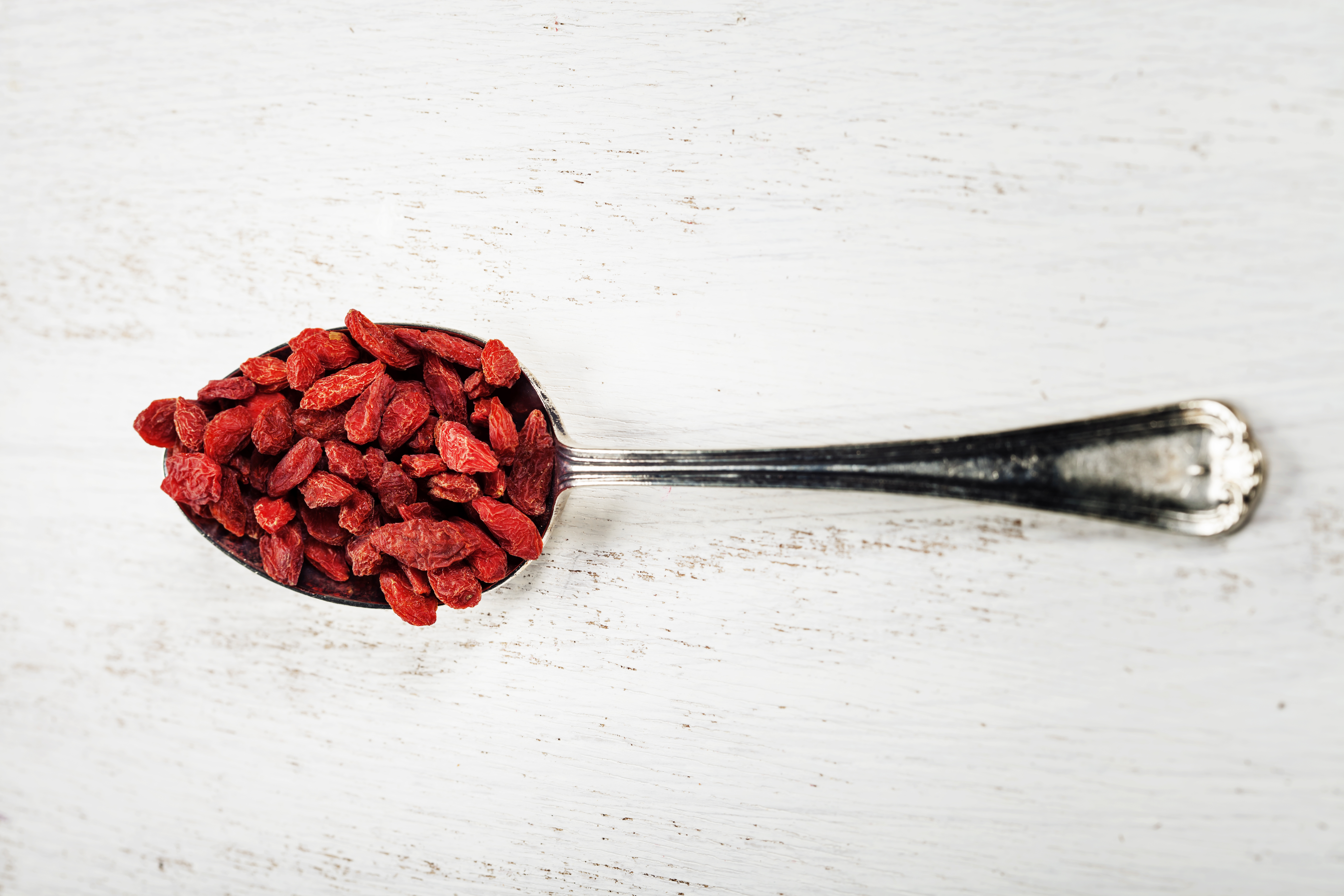Metal tablespoon of dried goji berries on wooden background